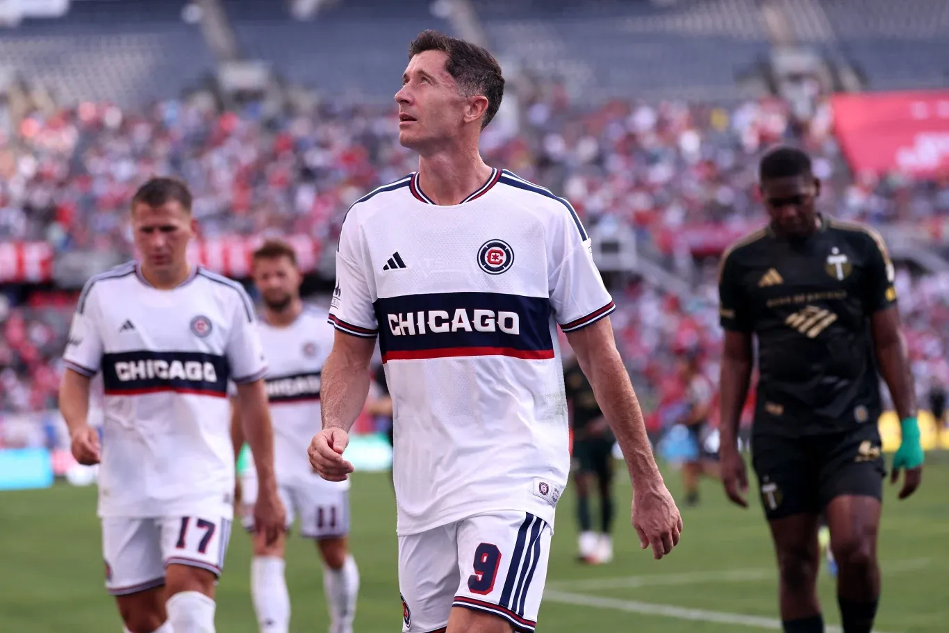 Robert Lewandowski i piłkarze Chicago Fire w białych strojach na boisku, w tle rywale i trybuny z kibicami.