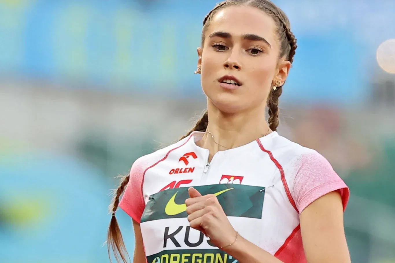 Lekkoatletka w biało-czerwonym stroju z numerem startowym podczas biegu na zawodach sportowych.