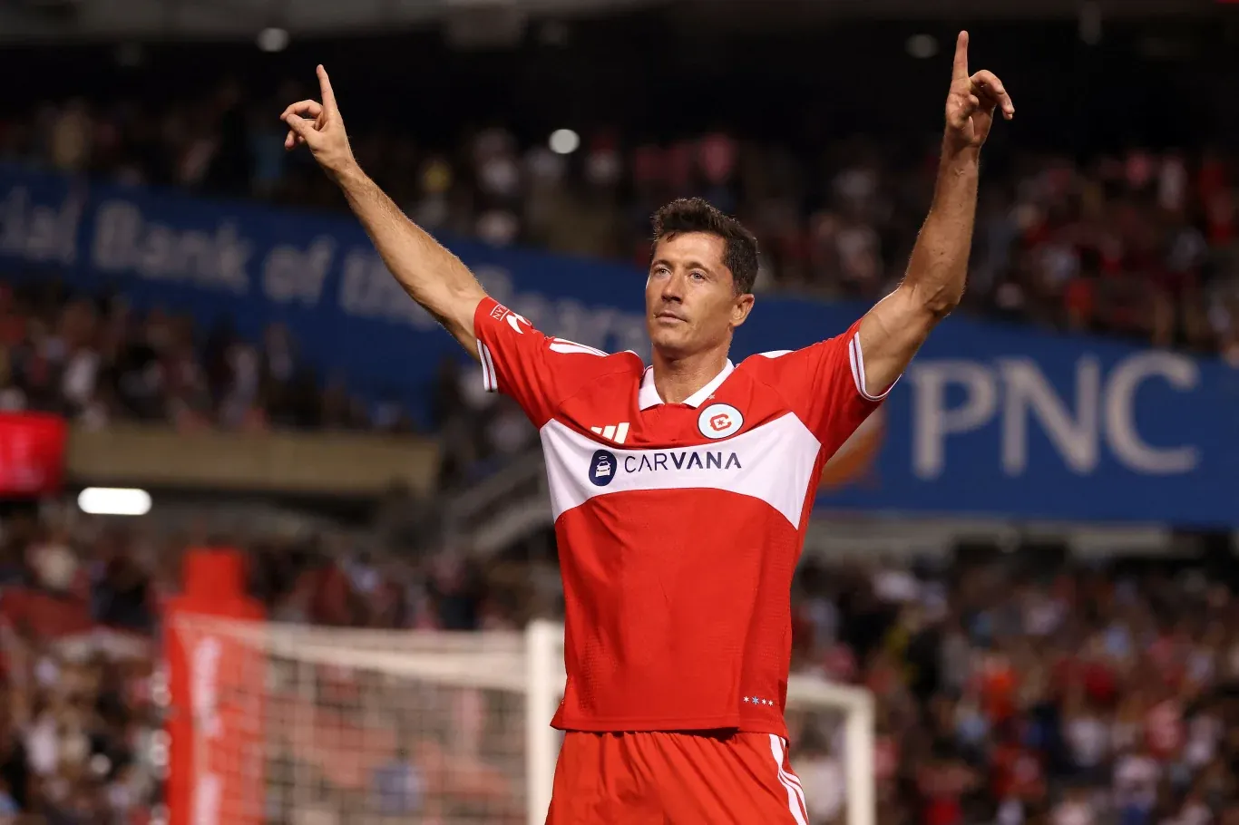 Robert Lewandowski w czerwono-białym stroju Chicago Fire unosi ręce po golu w meczu z Interem Miami, stadion w tle.